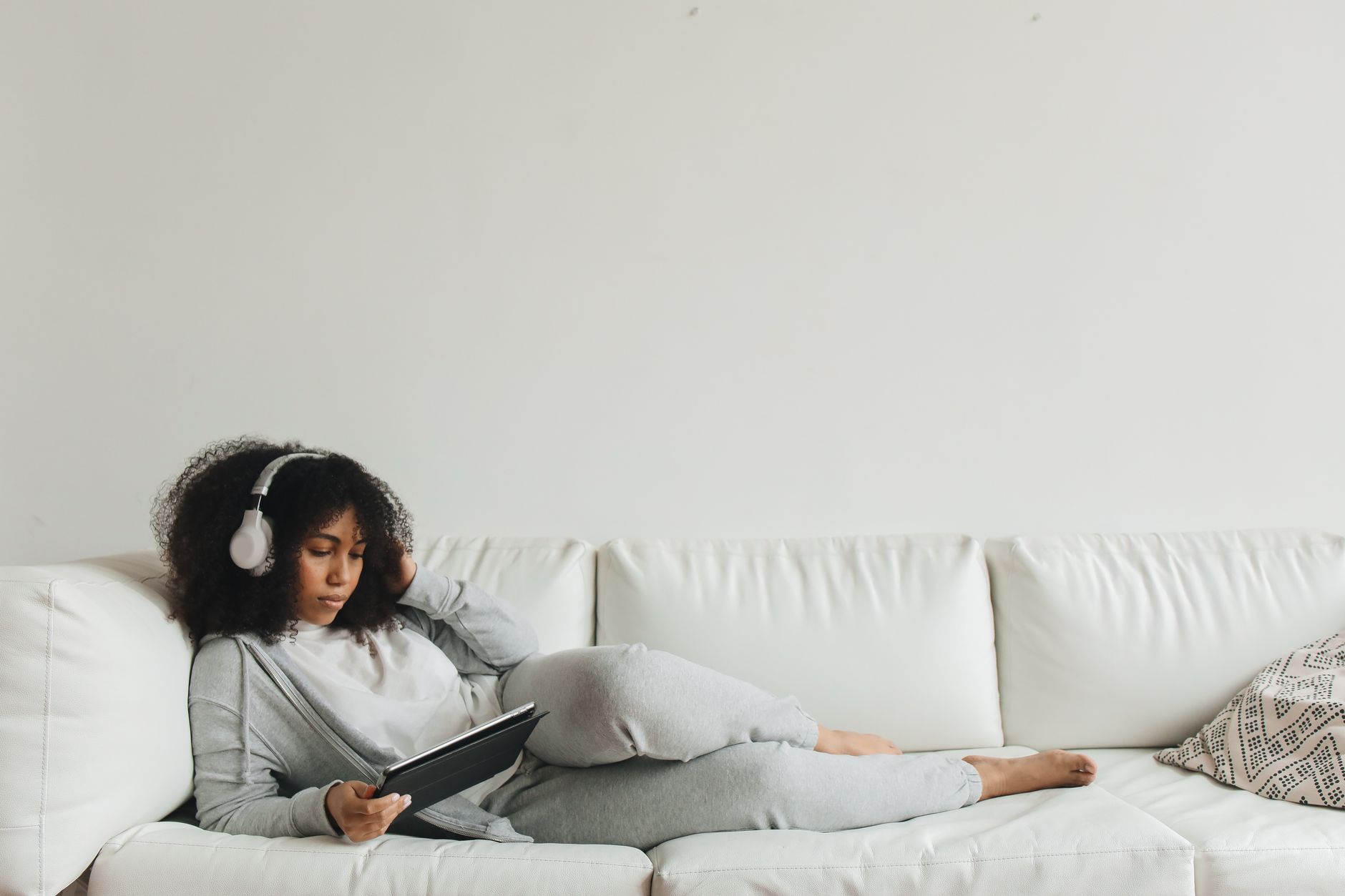 Young woman lying on a couch using a tablet and headphones. Perfect for technology and lifestyle themes.